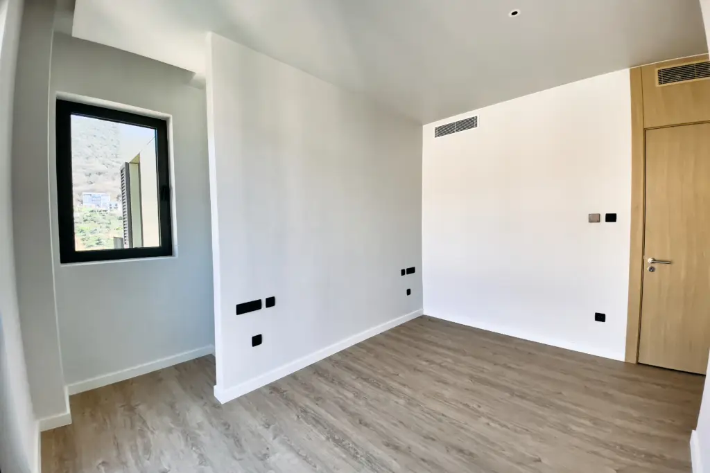 Empty room with wood flooring, white walls, window, and wooden door