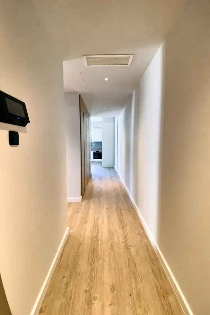 Long white hallway with wood flooring leading to a kitchen