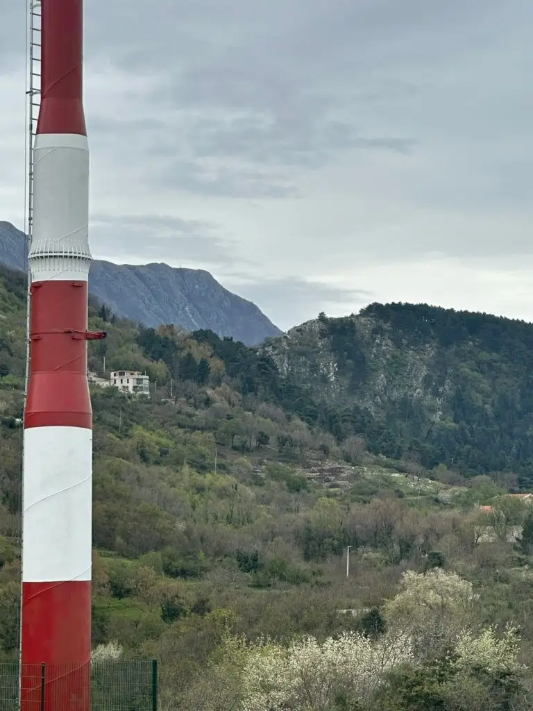 Red and white striped tower beside mountains and hillside