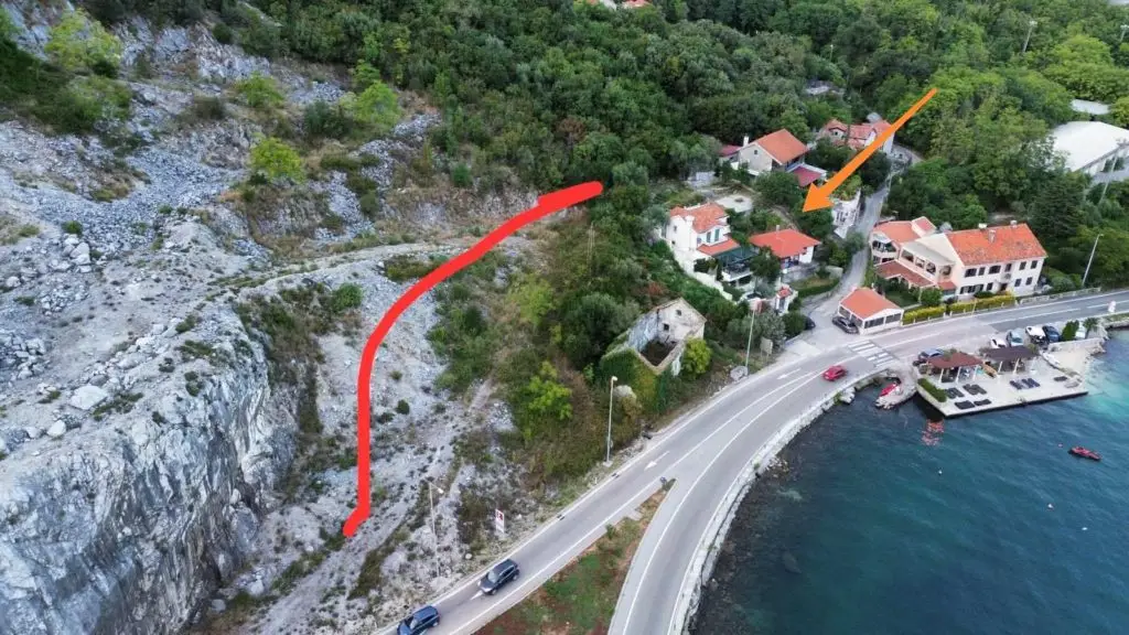 Aerial coastal road beside rocky hillside, marked plot and arrow