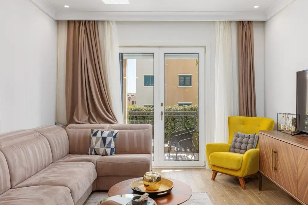 Living room with beige sofa, yellow chair, and balcony doors