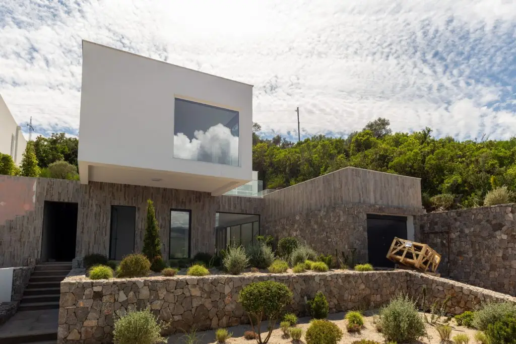 Modern white villa with stone walls and garden under cloudy sky