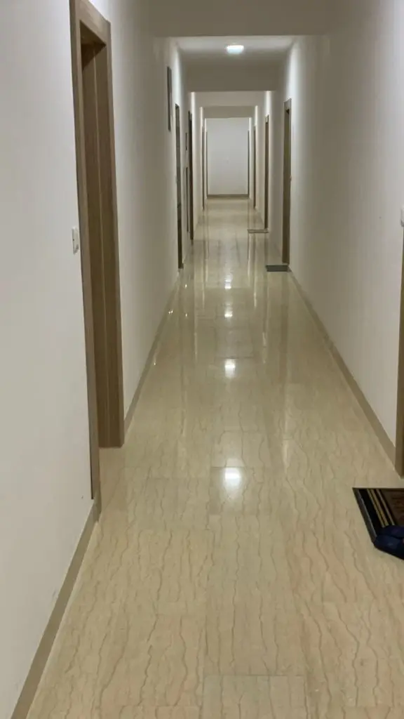 Long white apartment hallway with beige tiled floor and wooden doorframes