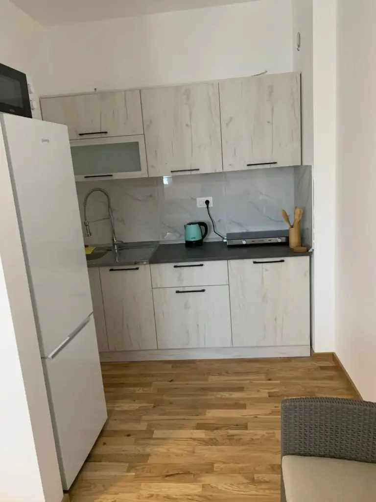 Compact kitchen with white cabinets, fridge, and kettle