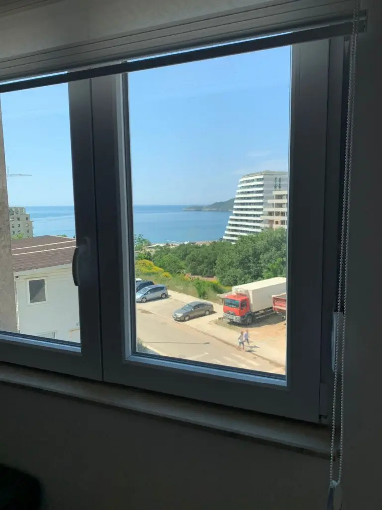Sea view through a window with buildings and parked cars