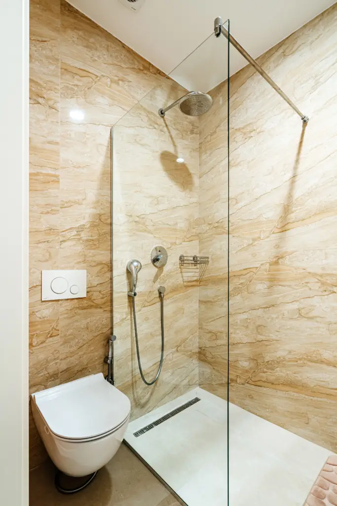 Modern bathroom shower with toilet and beige marble walls
