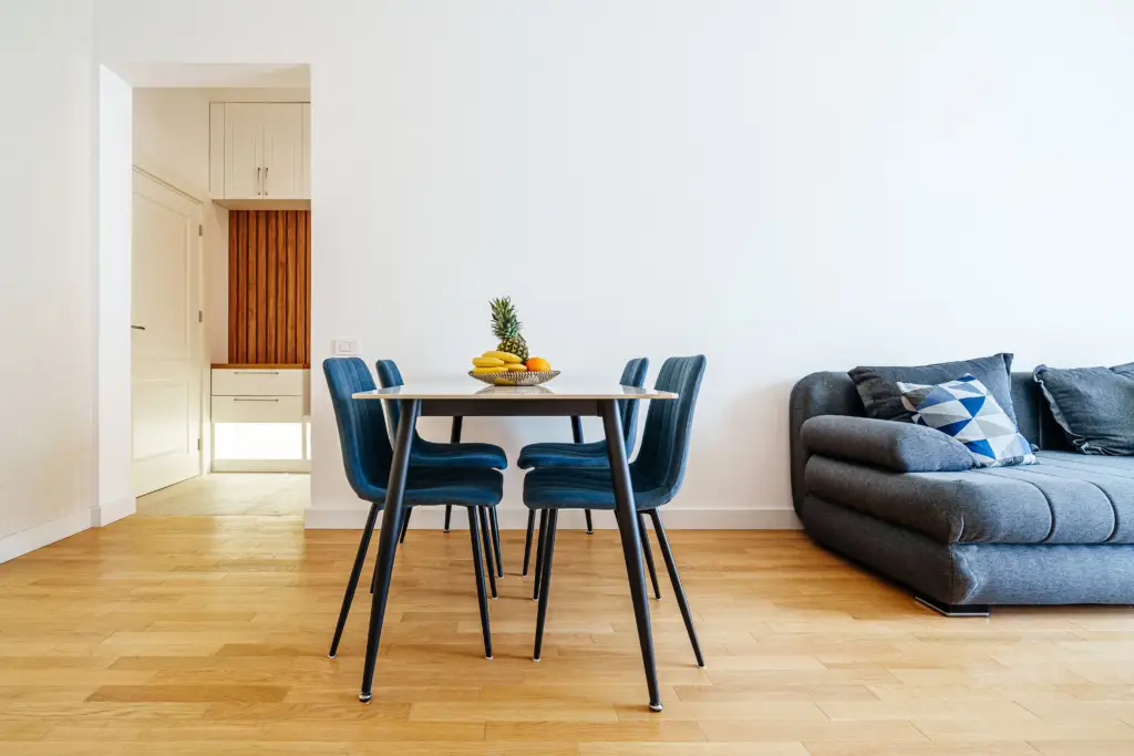 Dining table with blue chairs beside gray sofa and fruit bowl