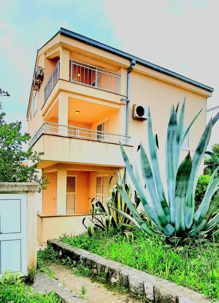 Two-story beige house with balconies and agave plants in front
