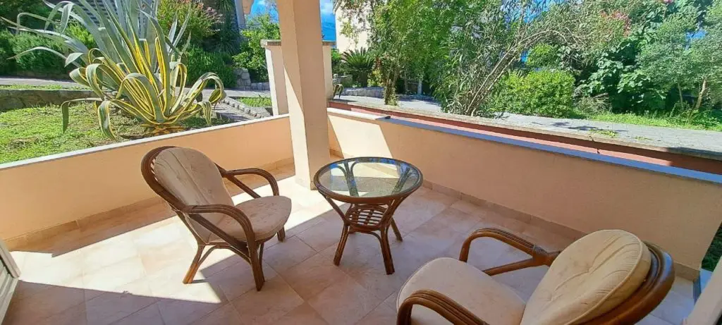 Covered patio with wicker chairs and glass table overlooking garden