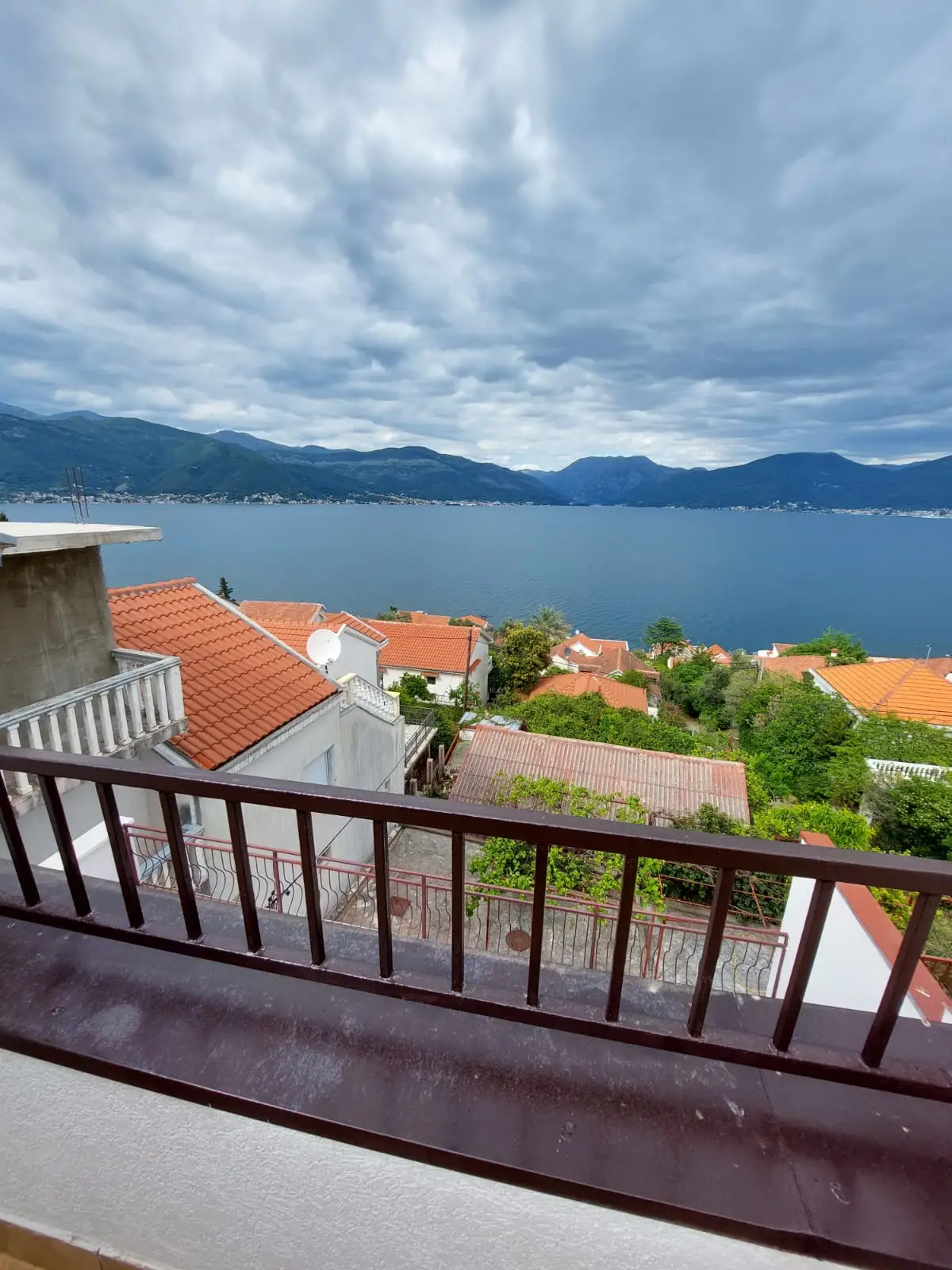 Balcony view over red-roofed houses and a bay with mountains
