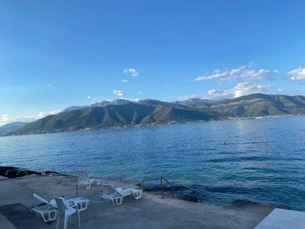 Sea view with mountains and white lounge chairs on concrete terrace