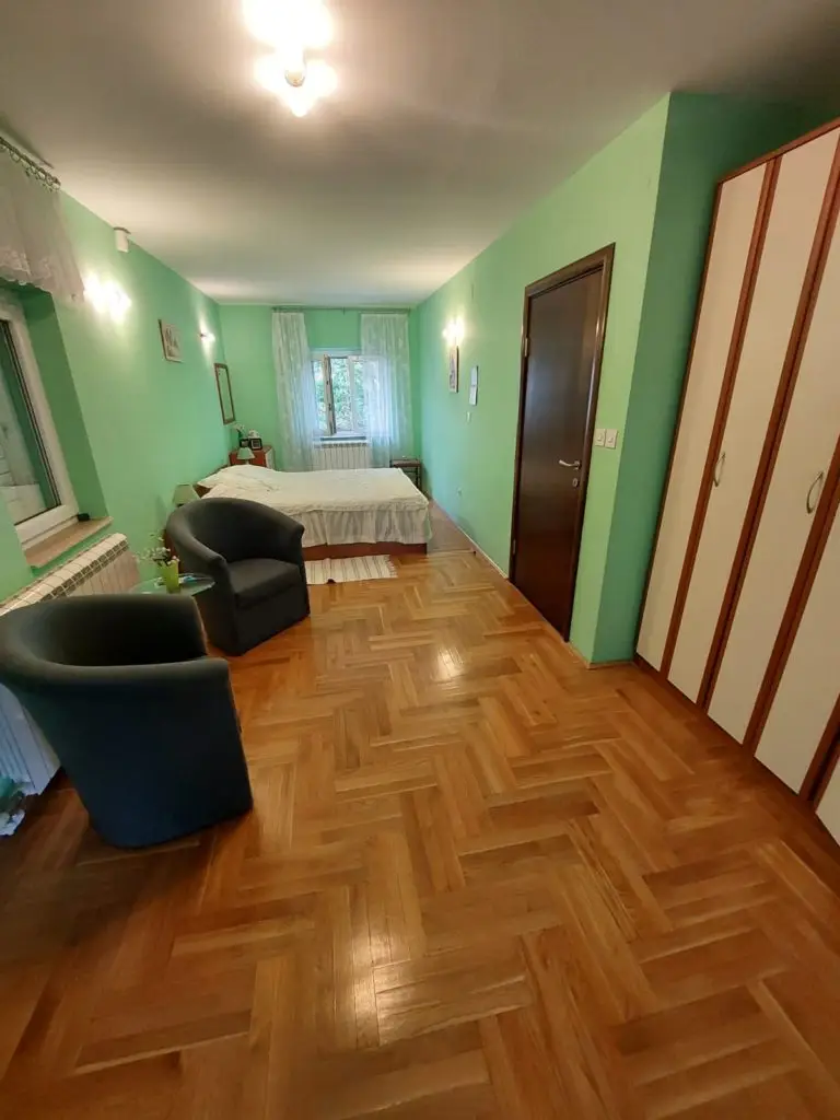 Green bedroom with bed, two dark chairs, and wardrobe