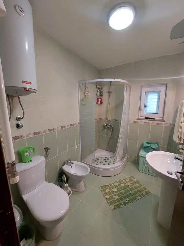 Green-tiled bathroom with shower, toilet, bidet, and sink