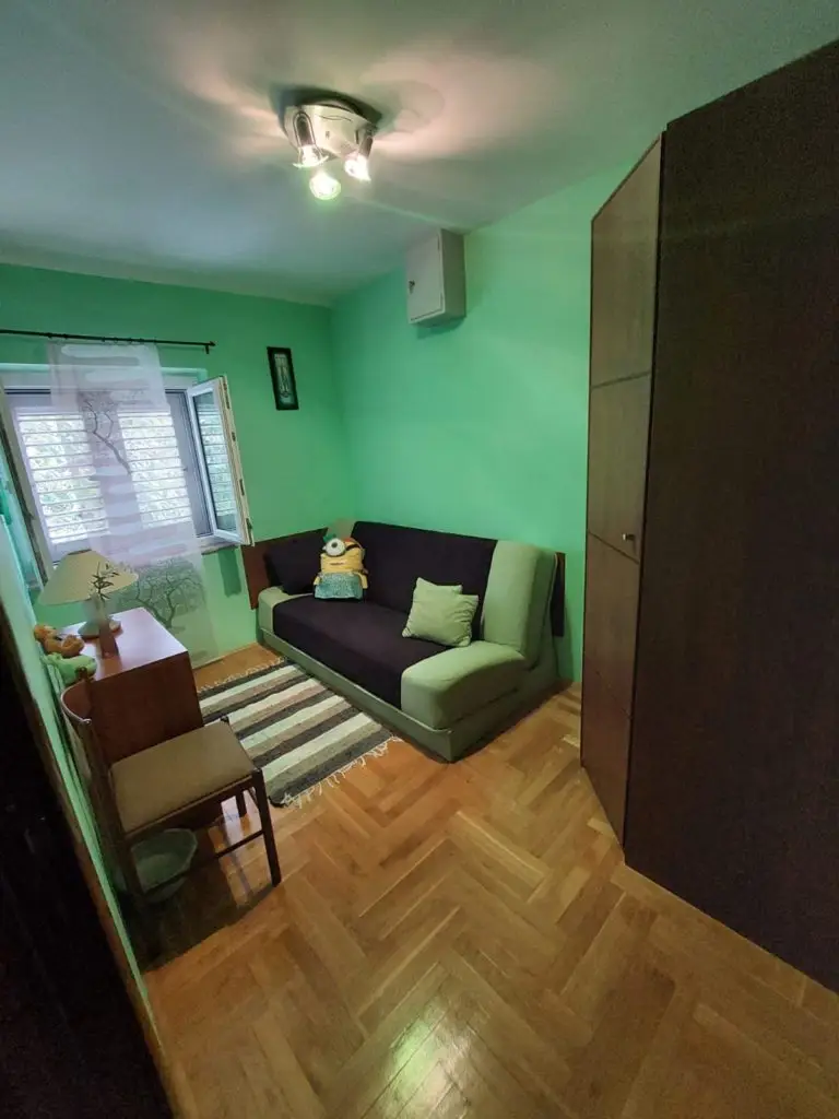 Small green bedroom with sofa, wardrobe, and window