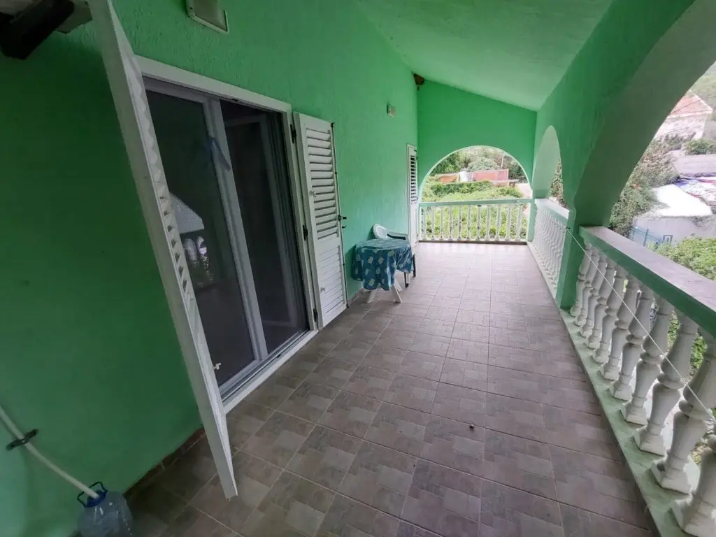 Green covered balcony with tiled floor and white railing