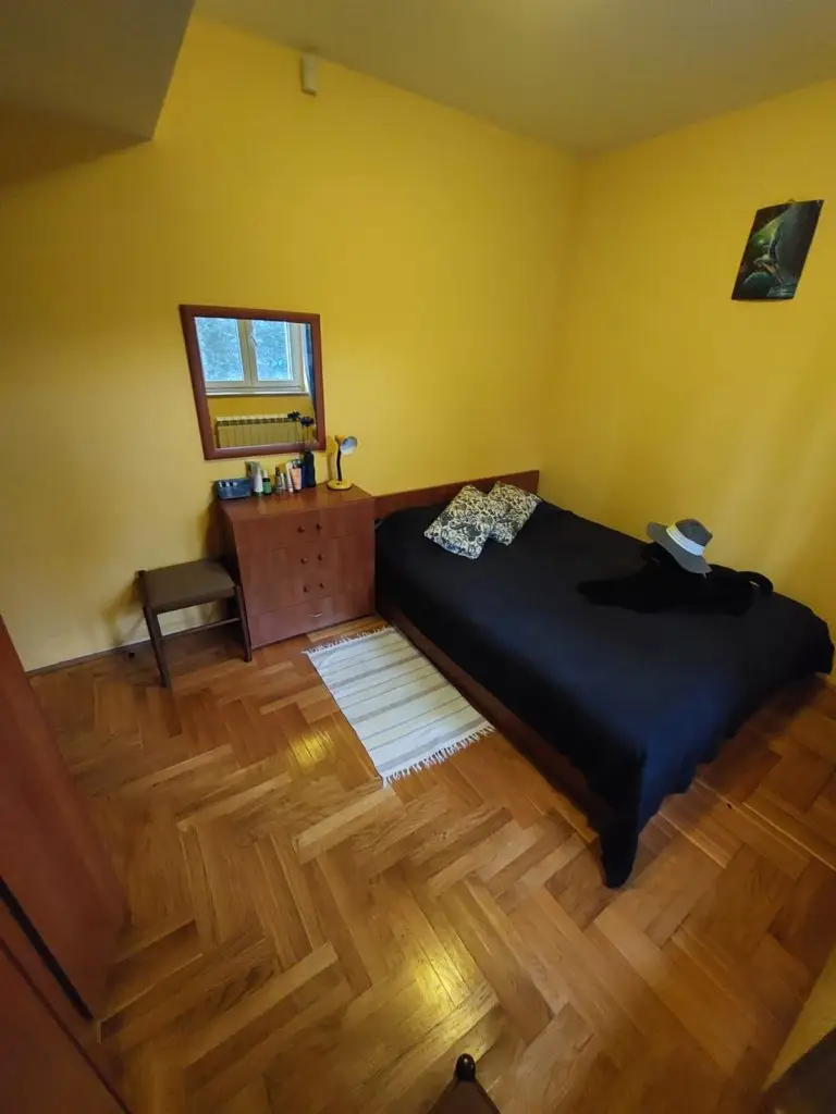 Yellow bedroom with black-covered bed, dresser, mirror, and stool