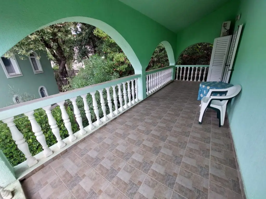 Green covered porch with arches, railing, and chair