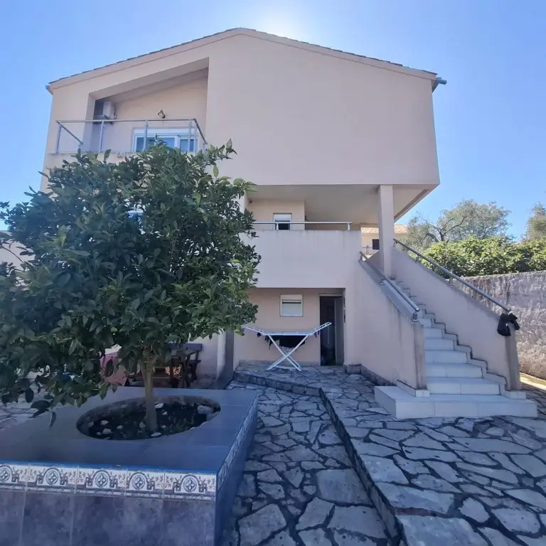 Beige two-story house with balcony, stairs, and stone courtyard