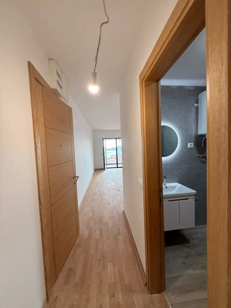 Narrow apartment hallway with wood floor, bathroom, and sea view at end