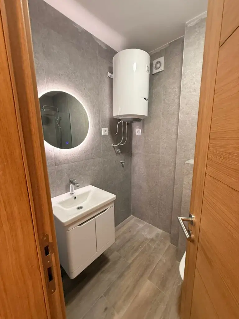 Small bathroom with sink, round mirror, and wall-mounted water heater