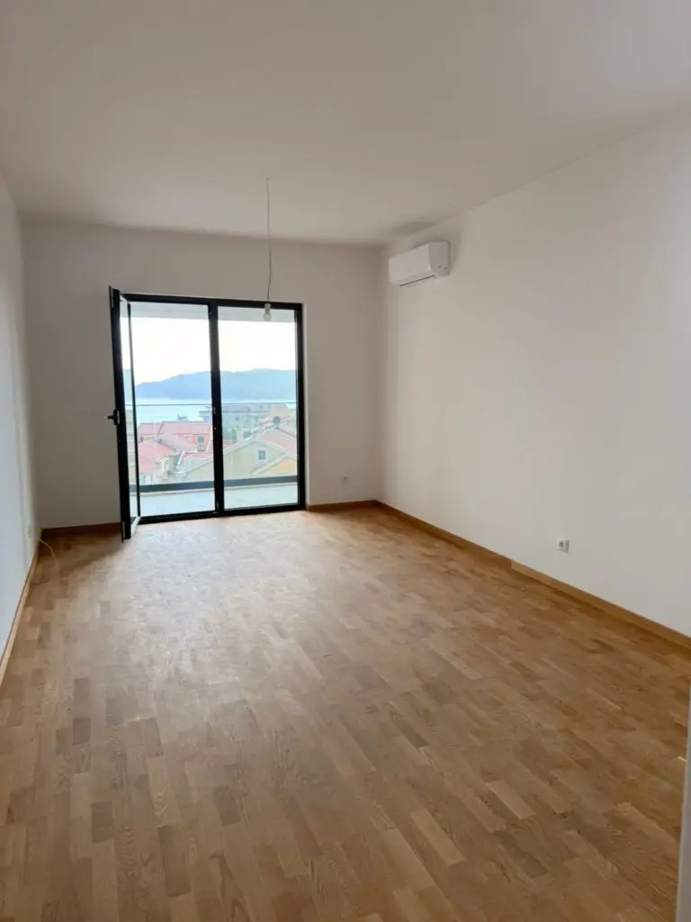 Empty room with wood floor, open balcony door, and sea view