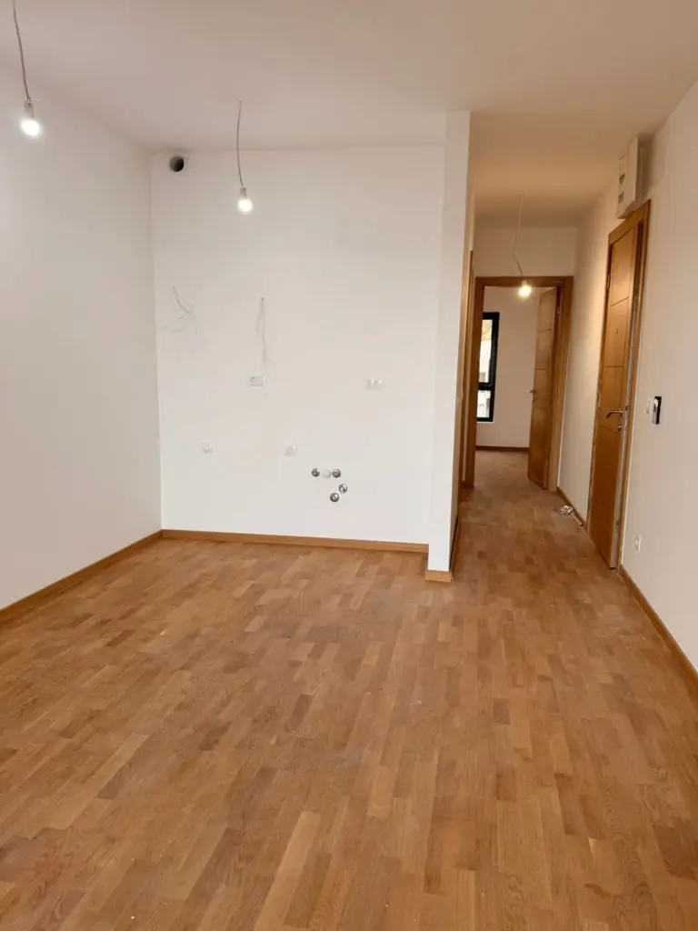 Empty room with wood flooring and hallway, white walls, hanging bulbs