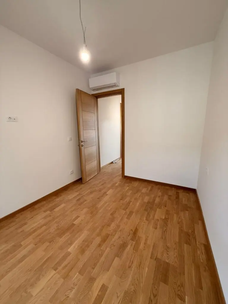 Empty room with wooden floor, open door, and wall-mounted AC