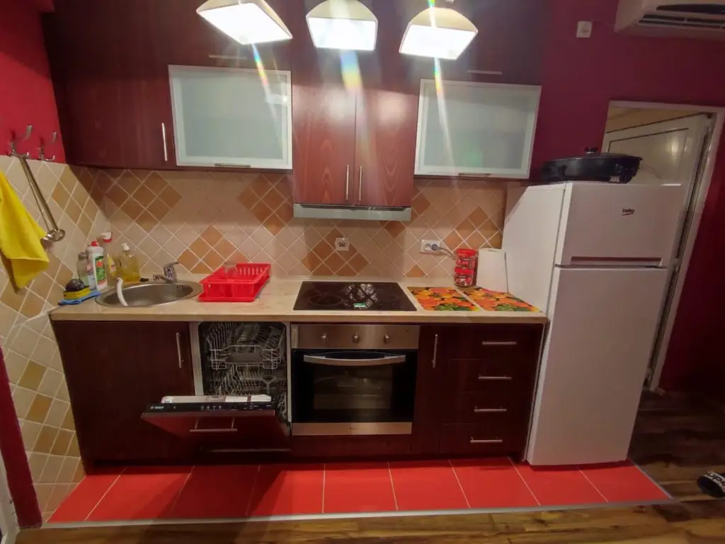 Compact kitchen with red cabinets, white fridge, and open dishwasher