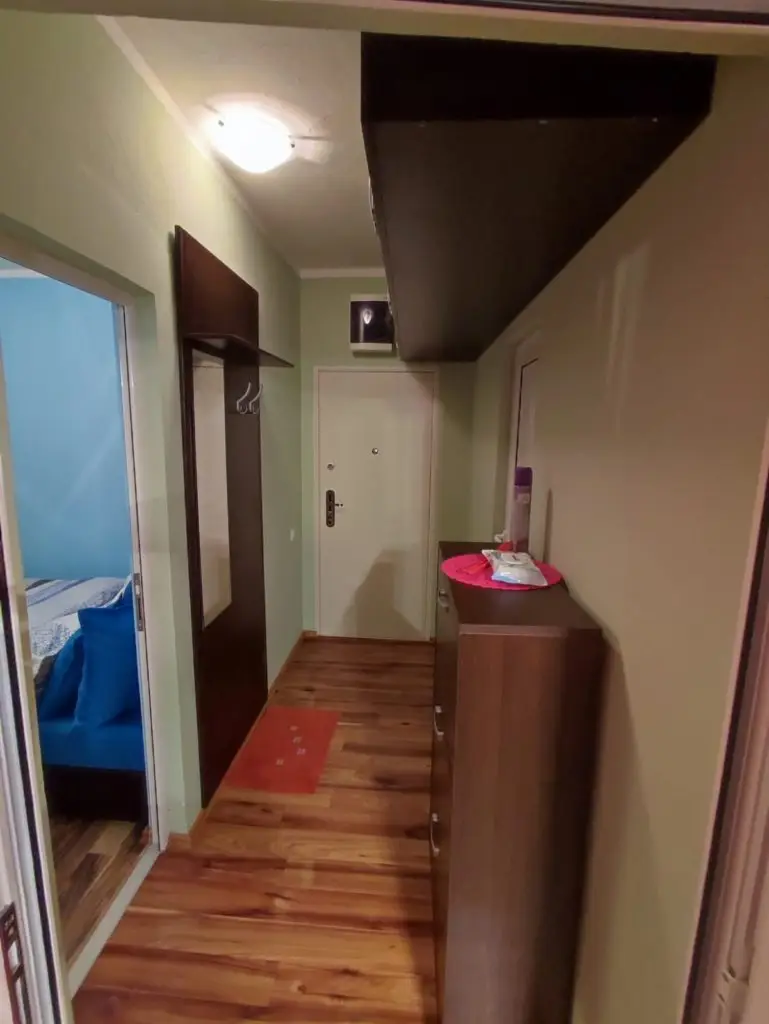 Narrow hallway with wooden floor, white door, and coat rack