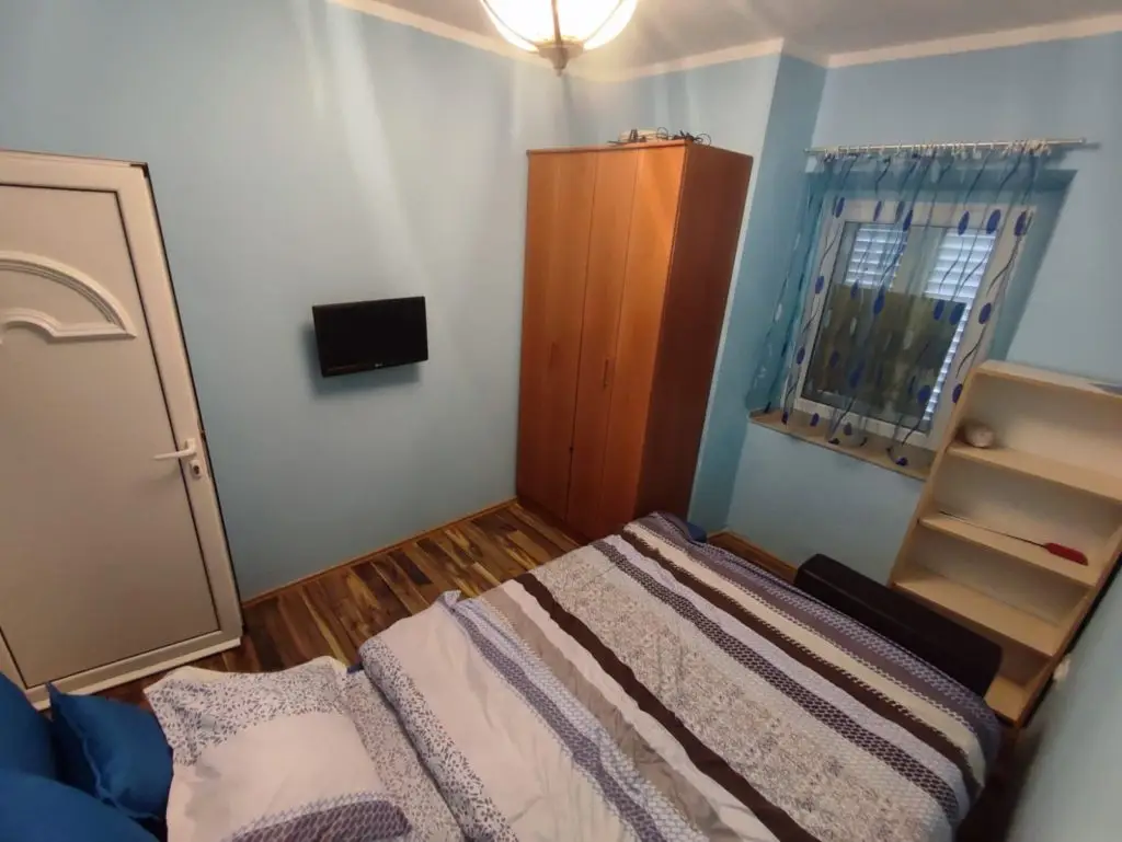 Small bedroom with bed, wardrobe, wall-mounted TV, and window