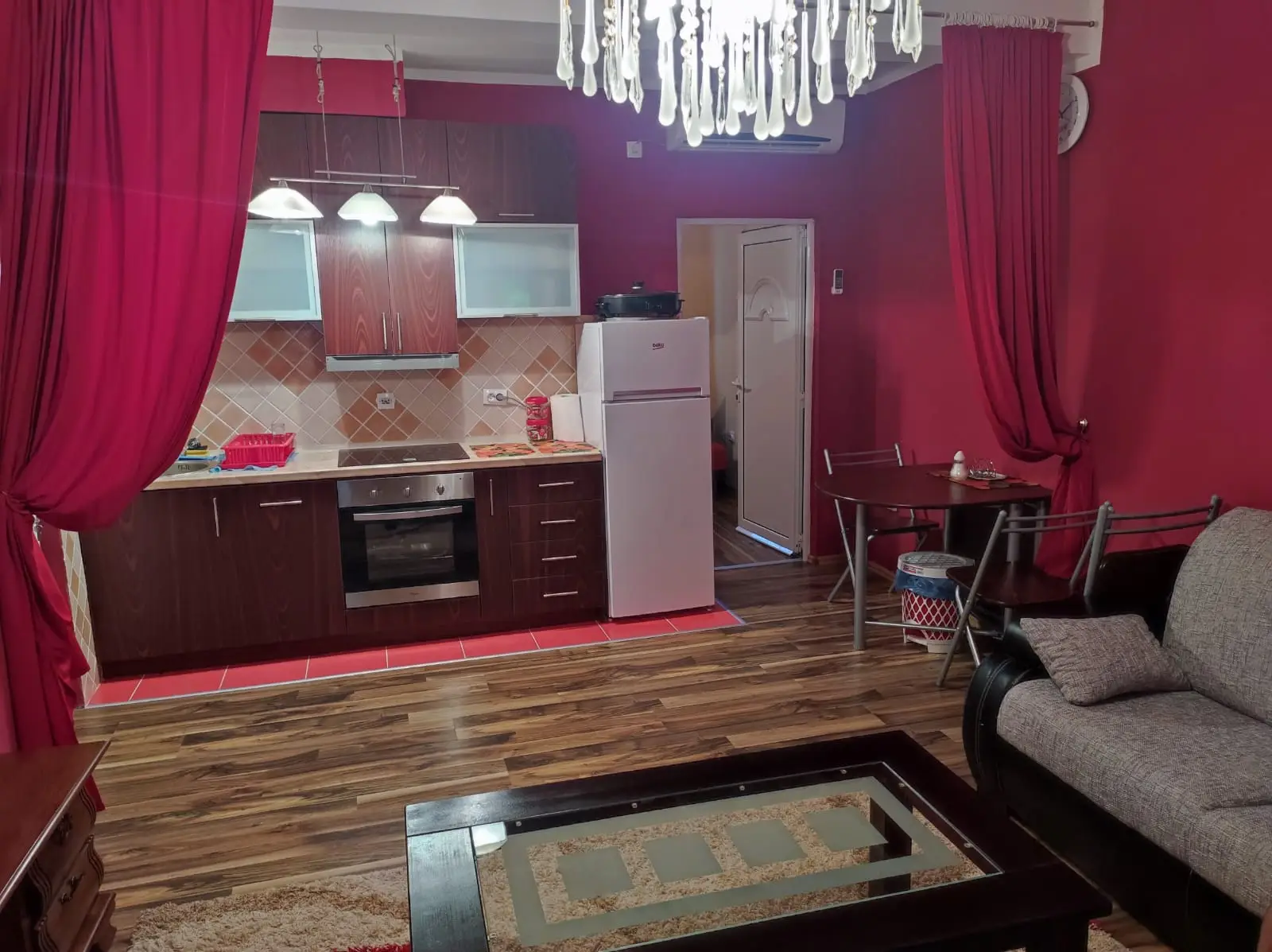 Red-curtained living room with kitchenette, sofa, and glass coffee table