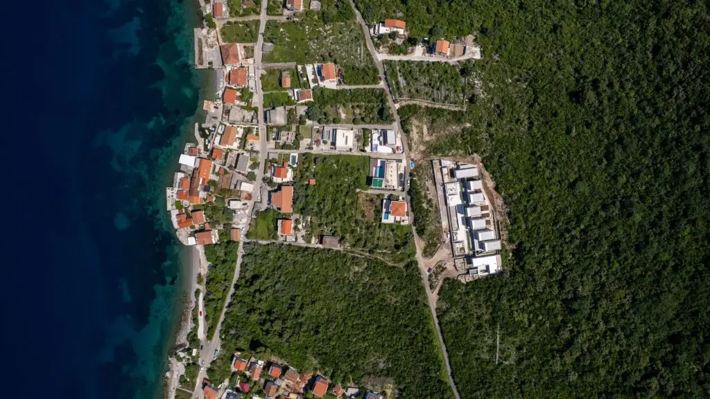 Aerial view of coastal houses beside a forested hillside