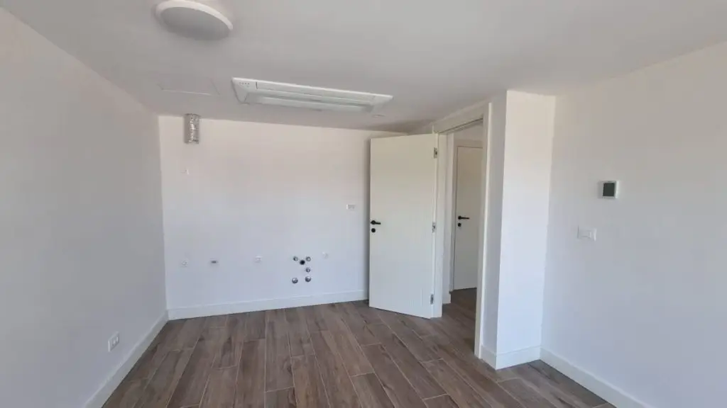Empty white room with wood-look floor and open door