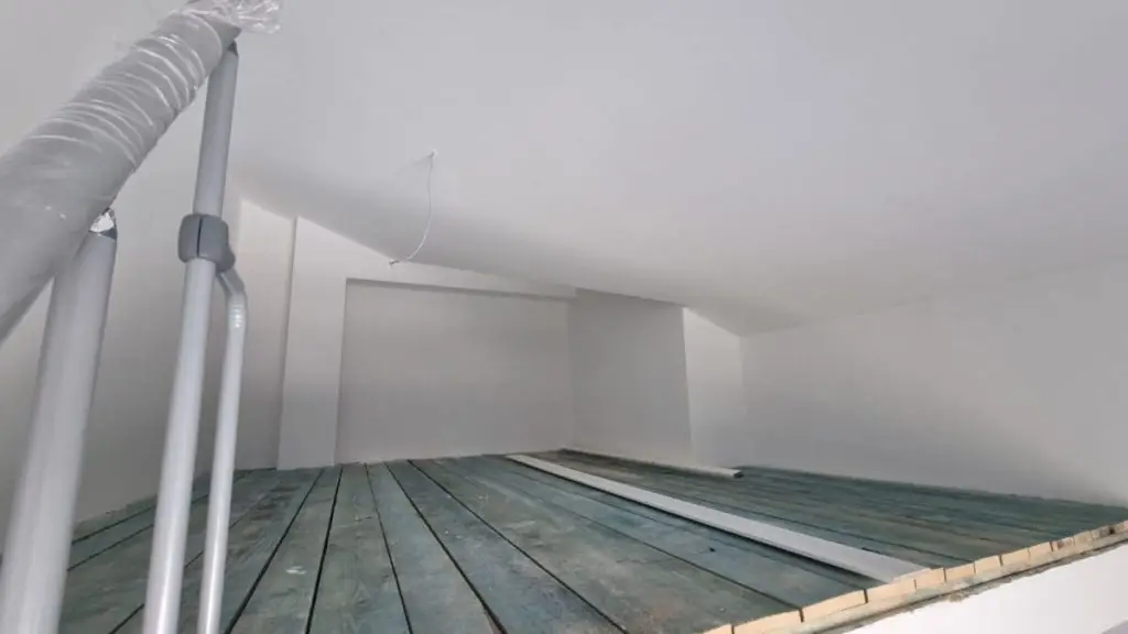 Unfinished attic storage space with sloped white ceiling and pipes