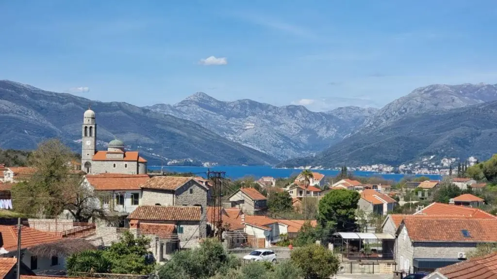Village rooftops with church tower, bay, and mountains