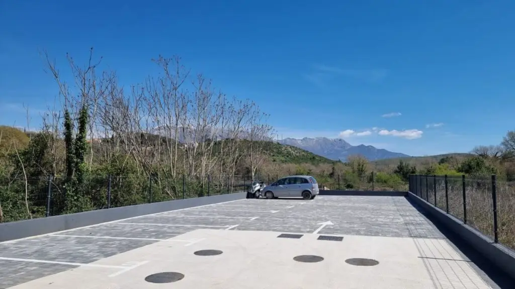 Empty parking area with a silver car and scooter, mountains beyond
