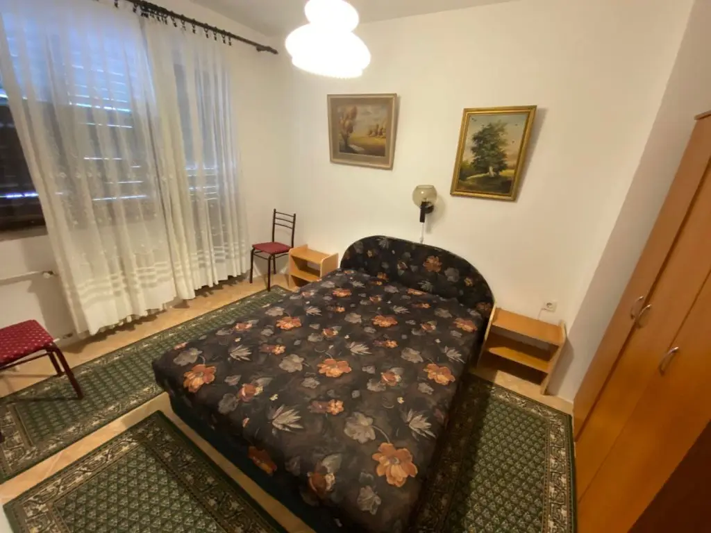 Bedroom with floral bedspread, wardrobe, chairs, and sheer curtains