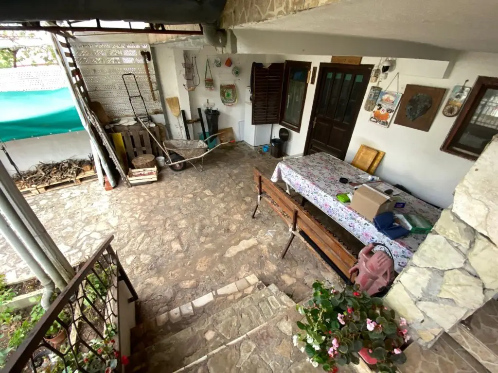 Covered stone patio with table, bench, wheelbarrow, and stairs