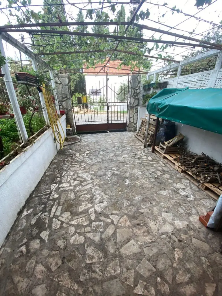 Stone-paved courtyard with metal gate and green tarp-covered wood stack