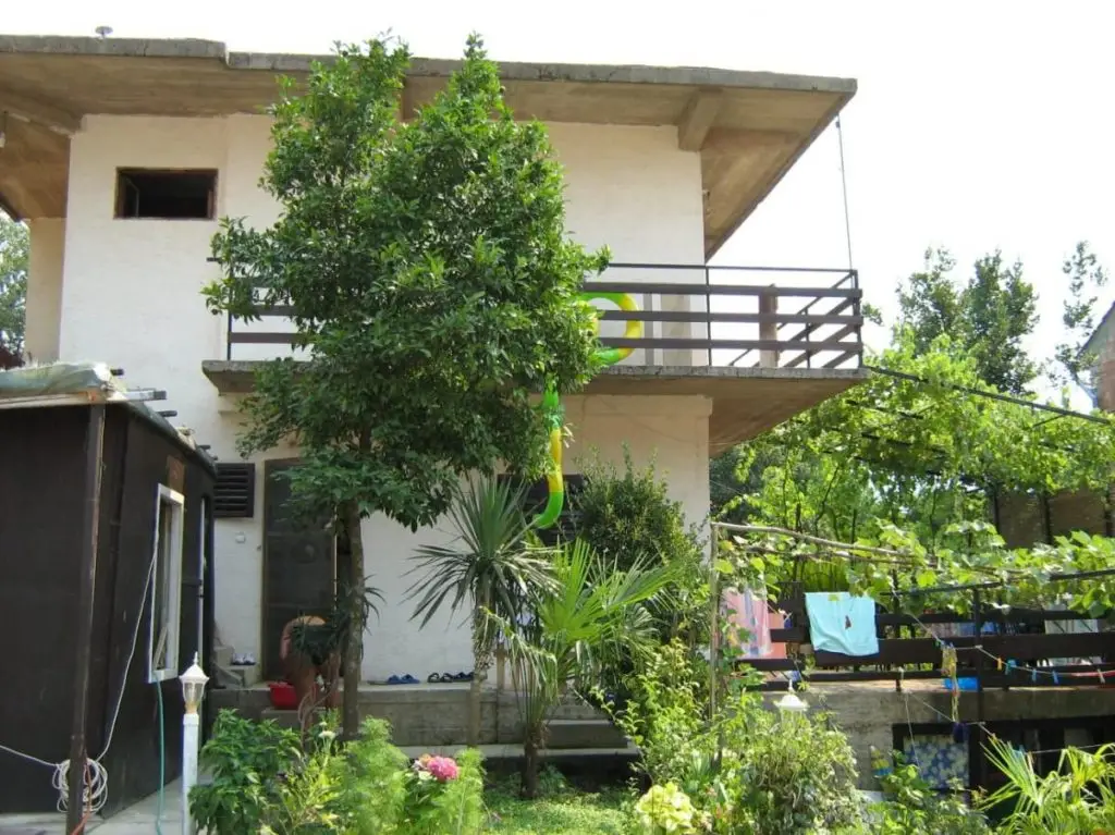 White two-story house with balcony and lush garden trees