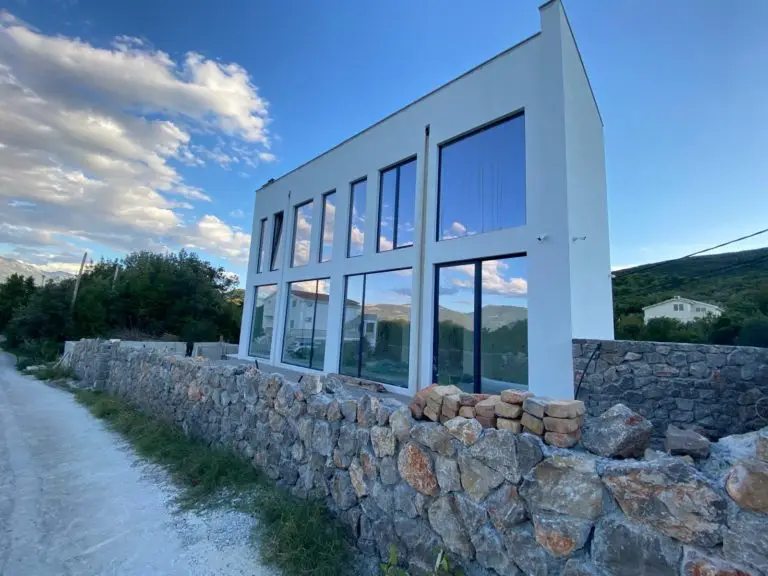 Modern white two-story house with large windows and stone wall