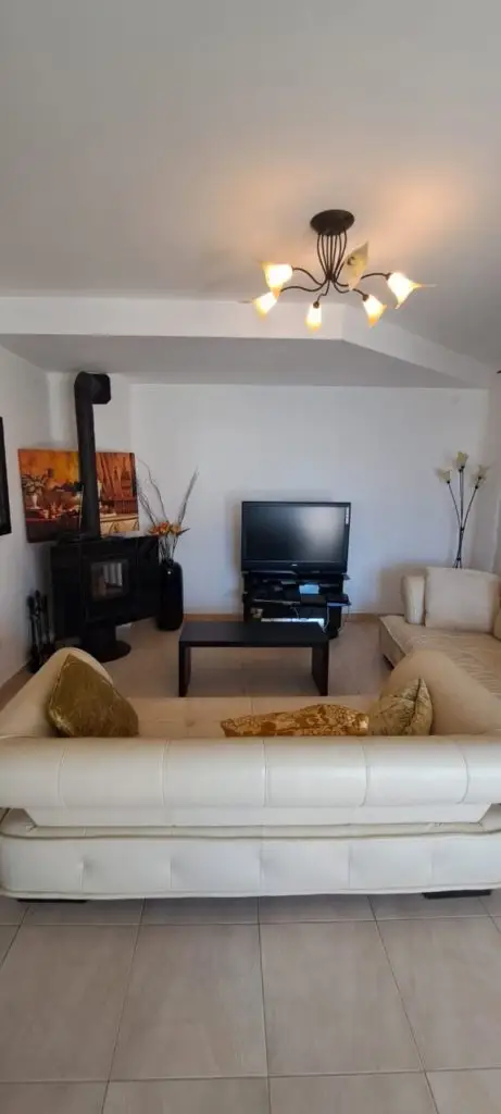 Living room with beige sofas, TV, and wood stove