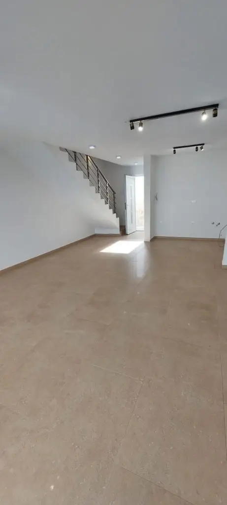 Empty modern room with beige tile floor, staircase, and open door