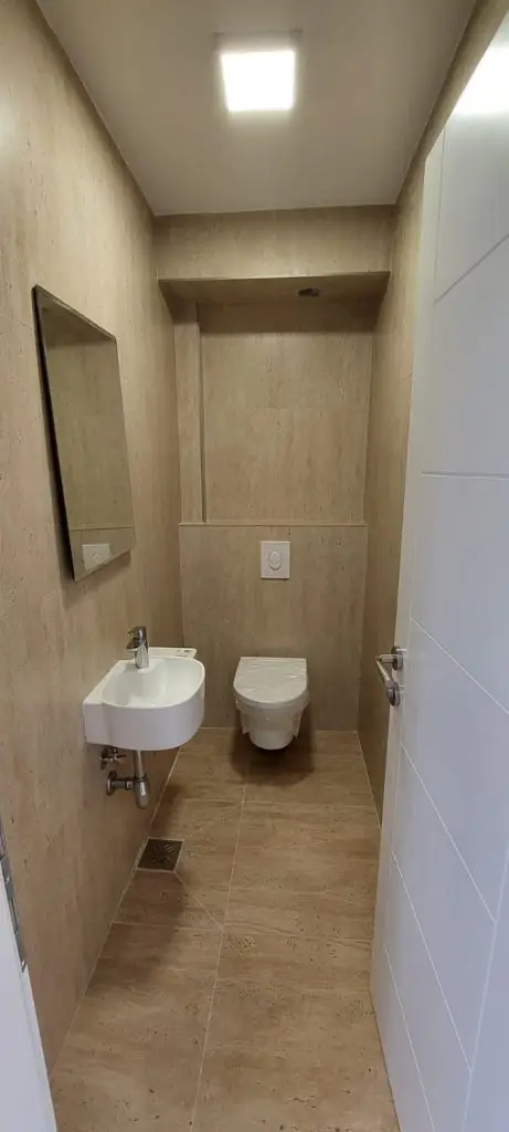 Narrow beige bathroom with sink, toilet, and mirror
