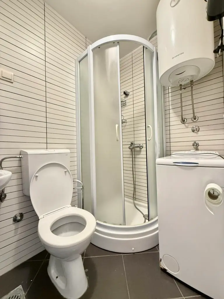 Small bathroom with toilet, shower, water heater, and washing machine