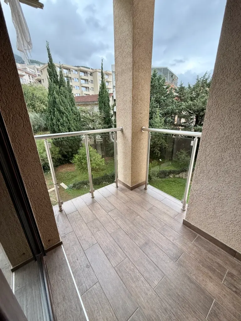 Covered balcony with glass railing overlooking trees and buildings