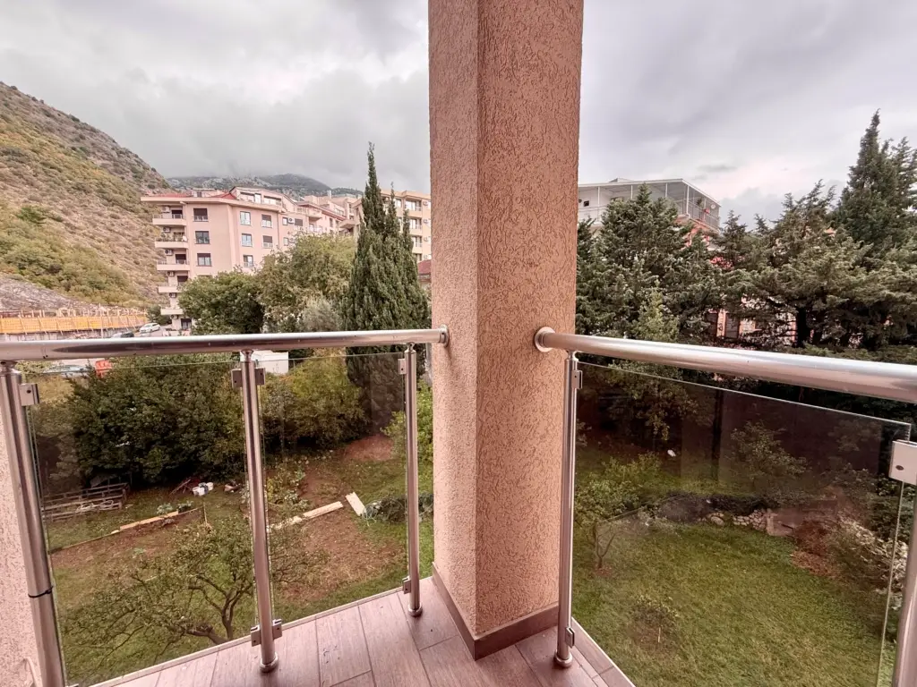 Balcony with glass railing overlooking trees and mountain buildings