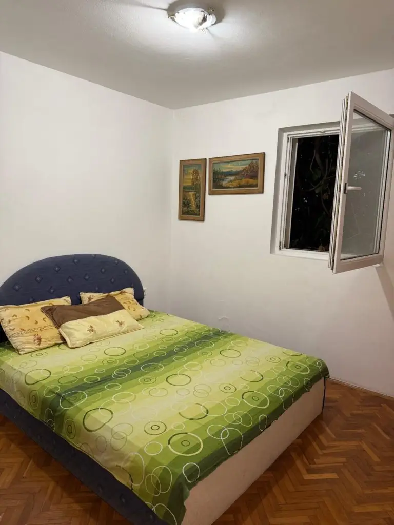 Bedroom with green bedspread, open window, and wall paintings