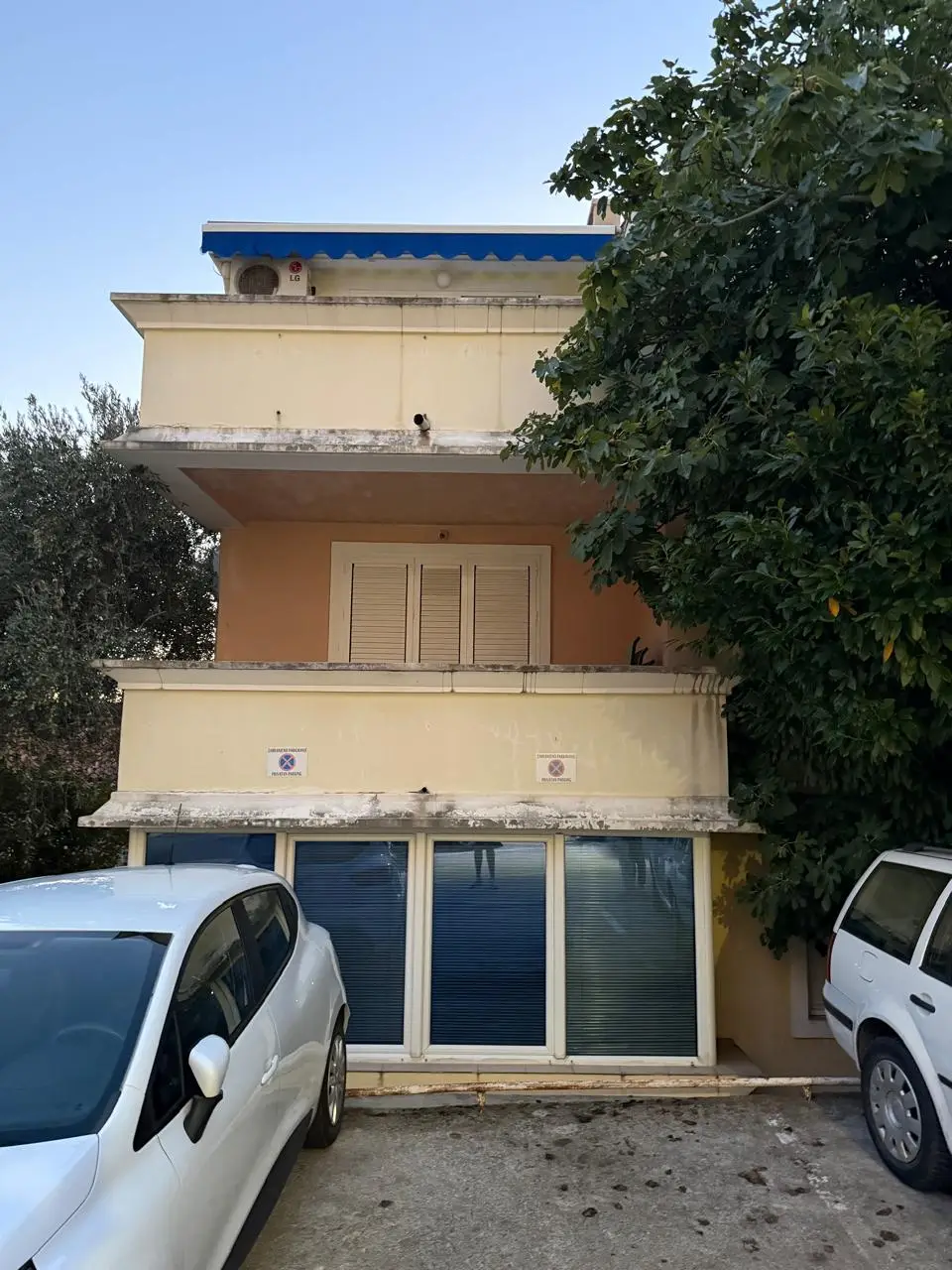 Beige apartment building with blue awning and parked cars