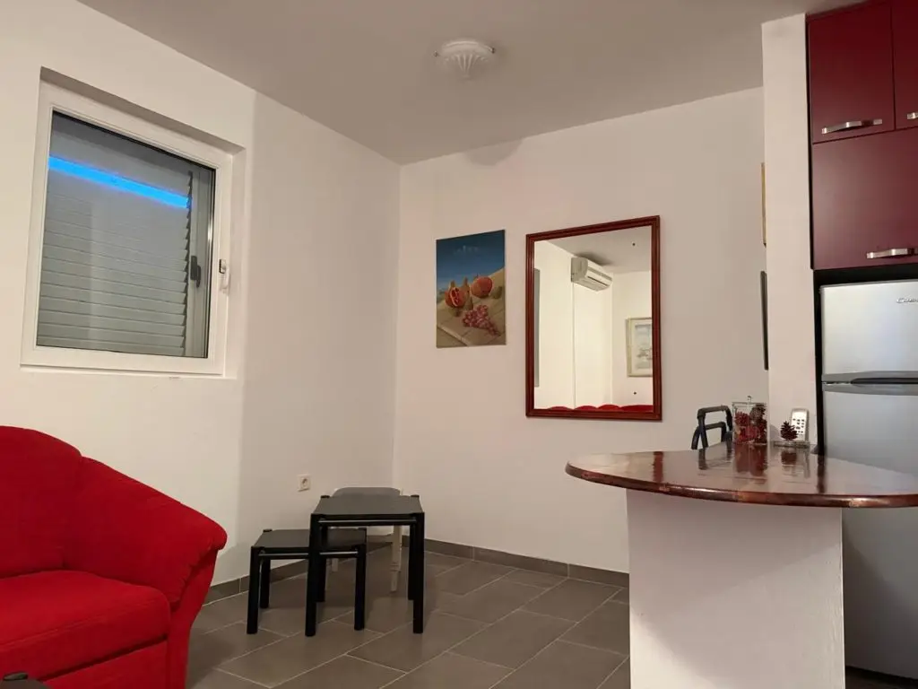Small studio room with red sofa, window, and kitchen counter